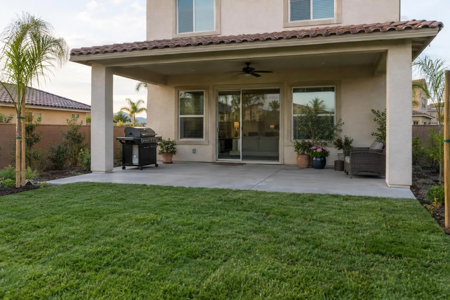 A level concrete patio beside a stucco house with palms and potted plants